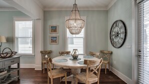 A dining room with a round table, chairs, a chandelier, and a wall clock.