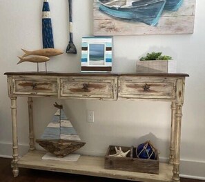 Una consola de madera rústica con cajones, un modelo decorativo de barco y un cuadro enmarcado en la pared superior.