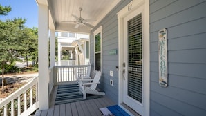 A porch with a welcome sign, a door with a number, and a covered area with chairs.