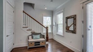 Un couloir avec un escalier en bois, un banc muni de paniers et un miroir accroché au mur.
