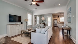 A spacious living room with a large sofa, a television, and a ceiling fan.
