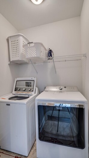 Un lavadero con una lavadora y secadora Maytag de carga frontal, un tendedero y una cesta blanca.