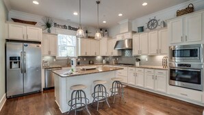 A kitchen with white cabinets, stainless steel appliances, a central island with stools, and pendant lighting.