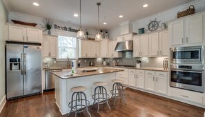 A modern kitchen with white cabinets, stainless steel appliances, a large island with bar stools, and pendant lighting.
