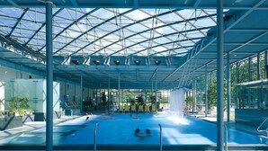 An indoor swimming pool with a glass ceiling, multiple lanes, and a seating area with yellow chairs. - Fantastic apartment in a prime location near Dresden at the gateway to Saxon Switzerland (Pirna)