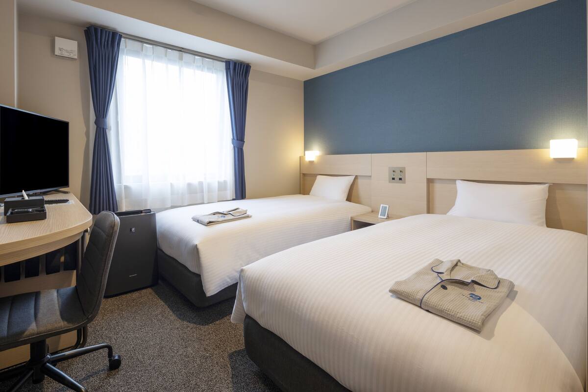 A hotel room with two beds, a desk with a computer, and a chair.