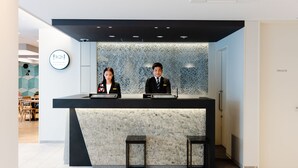 En receptionsdisk med två anställda, en skylt som visar att det finns ett privat rum, och en väggdekoration med geometriskt mönster.