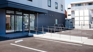 En modern byggnad med en entré av glas, ett takförsett utomhusområde med sittplatser och en parkeringsplats.