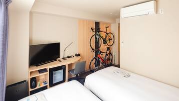 Quarto de hotel com duas camas, televisão, secretária com computador, cadeira e bicicleta fixada na parede.