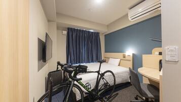 Habitación de hotel con cama, escritorio, silla, aire acondicionado y bicicleta.
