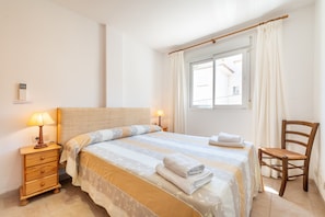 Ein Schlafzimmer mit einem Bett, Nachttischlampen, einem Sessel, einem Fenster mit Vorhängen und einem an der Wand montierten Thermostat.