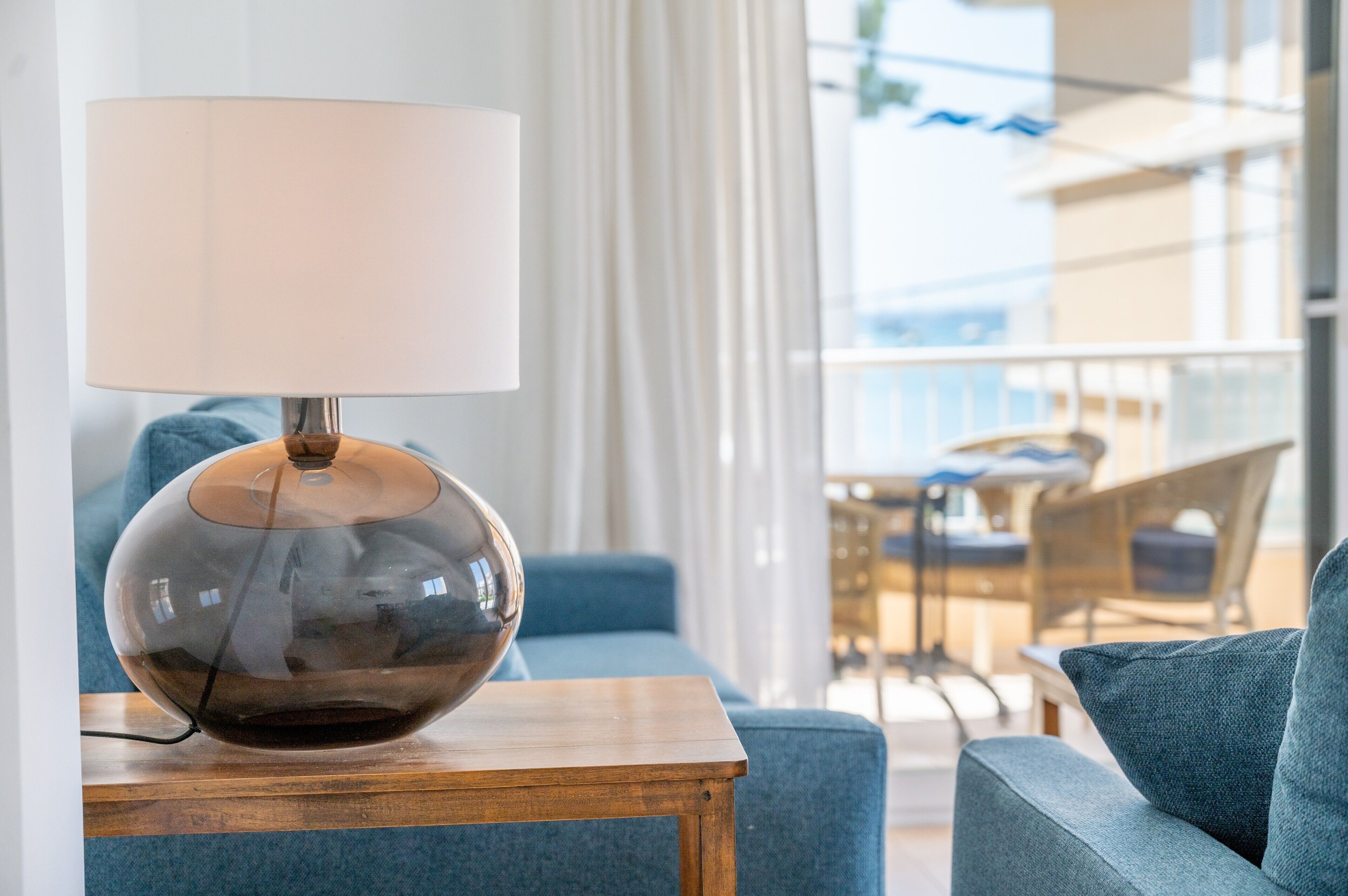 A modern room with a clear view of the balcony, a blue sofa, and a lamp on a wooden table.