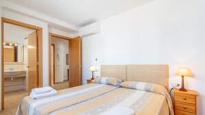 Un dormitorio con cama, mesitas de noche, lámpara y un baño visible a través de una puerta abierta.