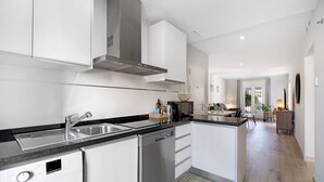 A modern kitchen with a dishwasher, sink, and stove, leading to a dining area with a table and chairs.
