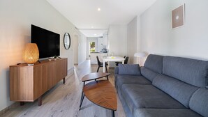 A modern living room with a sofa, TV, wooden cabinet, and a dining area in the background.