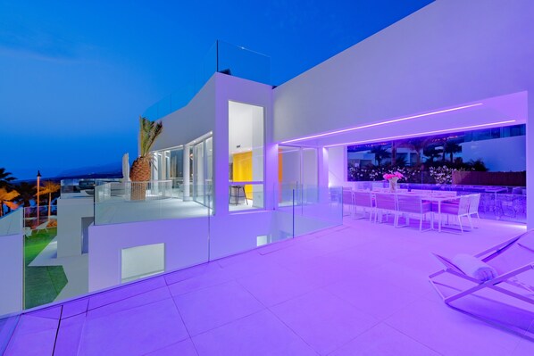 A modern outdoor patio area with glass railings, a seating arrangement, and a view of the surrounding landscape.
