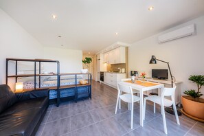 A modern living room with a sofa, a dining table with chairs, a TV, and a kitchen area with cabinets and appliances.
