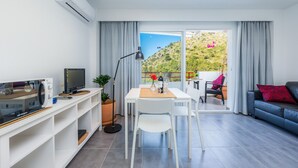 Een moderne woonkamer met een flatscreen televisie, een eettafel met stoelen, een bank en een groot raam met gordijnen.