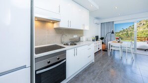 Een moderne keuken met witte kasten, een roestvrijstalen spoelbak en een oven. Er is een eethoek met een witte tafel en stoelen, en een uitzicht op een groen landschap door grote ramen.