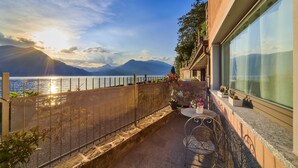 Un balcon avec vue sur un lac et des montagnes, une table avec des chaises et des plantes en pot.
