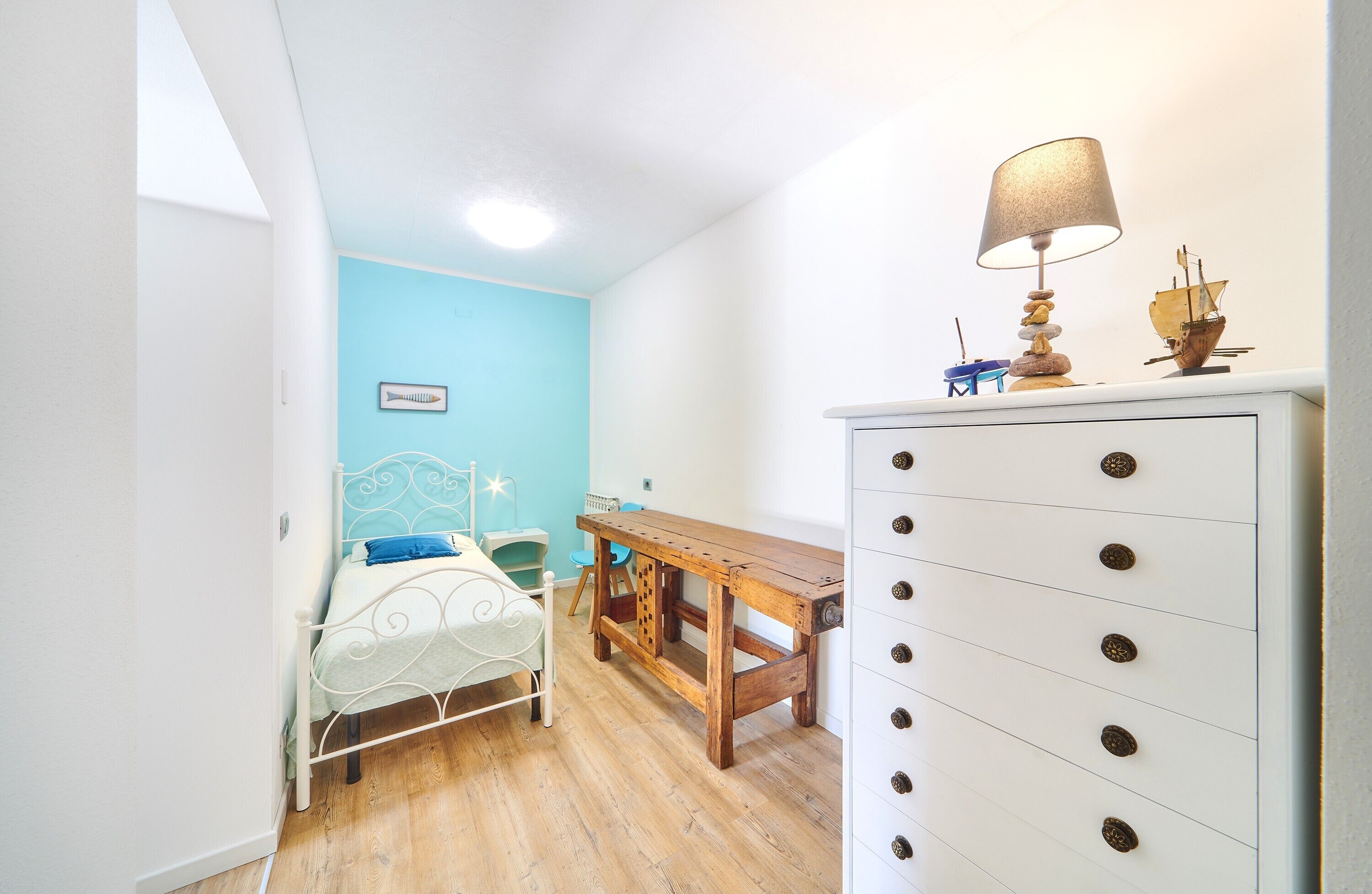 A bedroom with a bed, a wooden desk, a dresser, and a lamp.