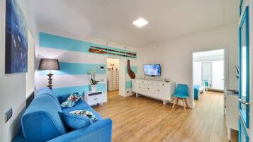 A living room with a blue sofa, a TV, a wooden cabinet, and a guitar.
