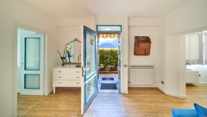 Une pièce dotée d’un plancher en bois, d’une commode blanche, d’un miroir, d’une porte à cadre bleu et offrant une vue sur la verdure et les montagnes par une porte ouverte.