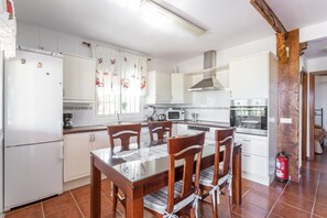 A kitchen with white cabinets, a dining table with chairs, a microwave, a stove, and a fire extinguisher. - Vacation Home Casita Puente Viejo with Pool, Wi-Fi, A-C, Terraces & Garden (NERJA)