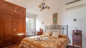 A bedroom with a large wooden wardrobe, a bed with a quilt, a bedside table, and a wall-mounted air conditioner.