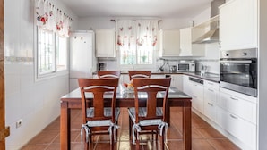 A kitchen with white cabinets, a dining table with chairs, a microwave, an oven, and a window with curtains.