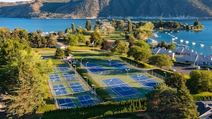 Een tennisfaciliteit met meerdere banen, omringd door bomen en uitzicht op een meer.