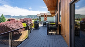 Een houten terras met buitenmeubilair, een barbecue en uitzicht op de bergen.