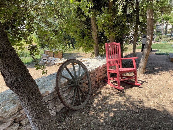 A rustic outdoor setting with a stone wall, a wooden wheel, and a red chair.
