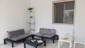 Ein Zimmer mit einer Sofagarnitur, einem Couchtisch, einem kleinen weißen Tisch und einer hohen Regaleinheit.