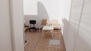 Ein kleiner, abgeschlossener Patio-Bereich mit gefliestem Boden, einem weißen Tisch, zwei Stühlen und einem schwarzen Grill.