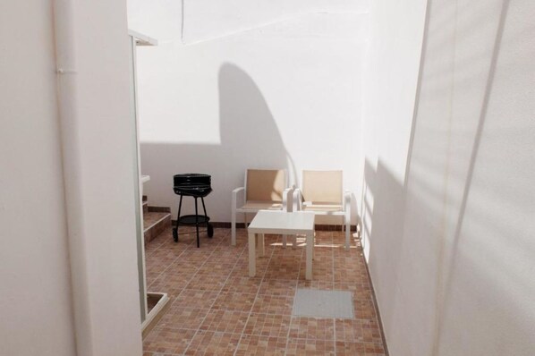 A small, enclosed patio area with a tiled floor, a white table, two chairs, and a black grill.