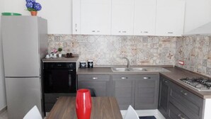 Eine kleine Küche mit weißen Schränken, einem Edelstahlkühlschrank, einem Gasherd und einer gefliesten Spritzschutzwand.