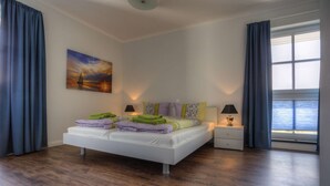 A modern bedroom with a large bed, two bedside tables, a nightstand, a painting, and a window with curtains. - Villa Namenlos - Holiday apartment 5 (Börgerende-Rethwisch)