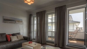 A modern living room with a sofa, coffee table, and a view of a balcony. - Villa Namenlos - Holiday apartment 5 (Börgerende-Rethwisch)