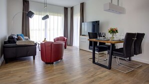 A modern living room with a sofa, red chairs, a dining table with chairs, a TV, and a wooden floor. - Villa Zeitlos - Holiday apartment 1 (Börgerende-Rethwisch)