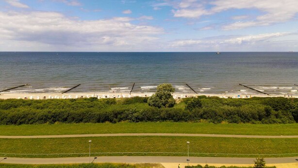 Udsigt over kysten med strand, græsareal og klar himmel.