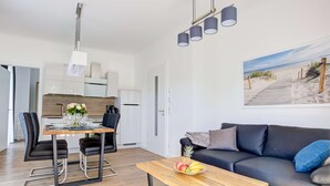 En moderne stue med et træsofabord, en sort lædersofa og et spiseområde med bord og stole.