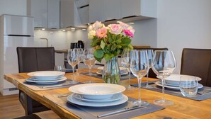 Uma mesa de jantar posta com pratos, copos e um vaso de flores em uma cozinha moderna com armários e uma máquina de café.