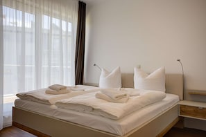 A neatly made bed with folded towels, a bedside table, and a lamp.