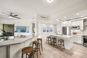A modern kitchen with white cabinetry, a central island with stools, stainless steel appliances, and artwork on the walls.