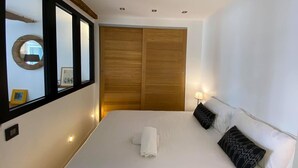 A bedroom with a large bed, a wooden wardrobe, a round mirror, and a bedside lamp. - Comfy Pinoche Proche Plage (Saint-Malo)