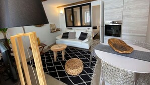 A modern living room with a sofa, a round coffee table, and a dining area with a table and chairs. There is a kitchen area with an oven and a refrigerator. - Comfy Pinoche Proche Plage (Saint-Malo)