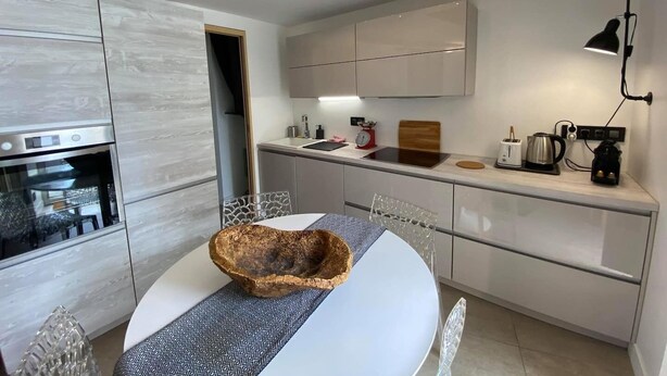 A modern kitchen with a built-in oven, a dining table with a decorative bowl, and a coffee machine. - Comfy Pinoche Proche Plage (Saint-Malo)