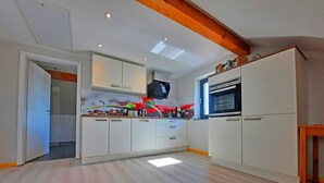 Una cocina moderna con armarios blancos, horno empotrado y televisor sobre la encimera.