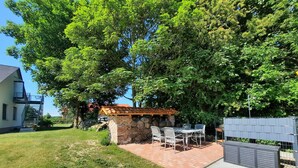 Un patio con pared de piedra, una pérgola de madera y una mesa con sillas.